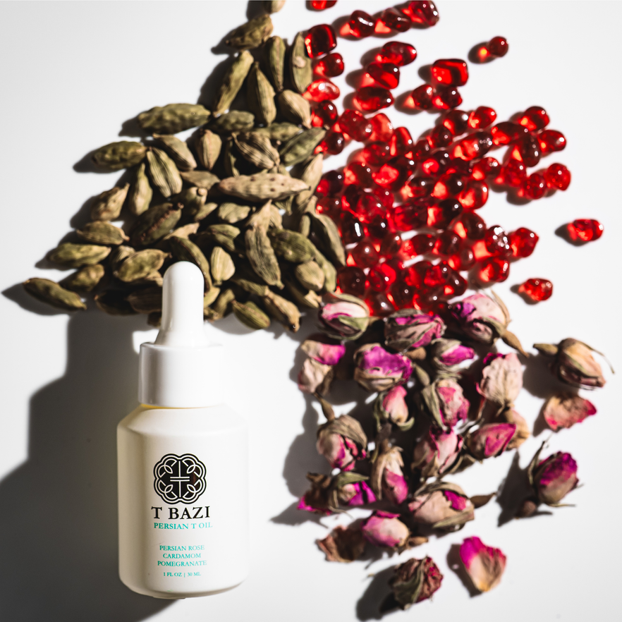 T Bazi Persian T Oil dropper bottle surrounded by cardamom pods, pomegranate seeds and dried rose buds