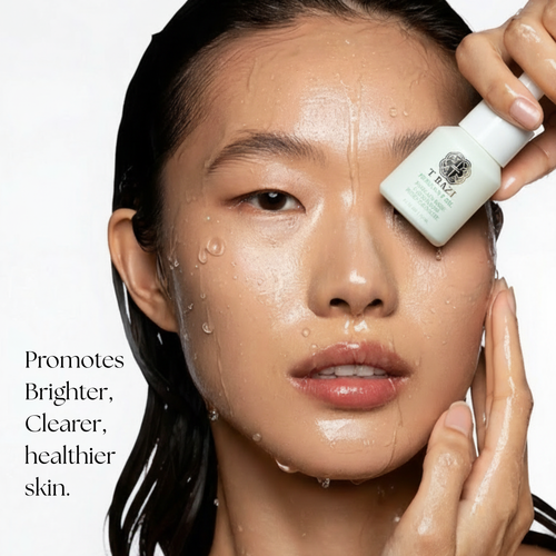 A close-up of a woman with wet, glistening skin holding a small white bottle near her eye. Text on the left reads, 'Promotes Brighter, Clearer, healthier skin.