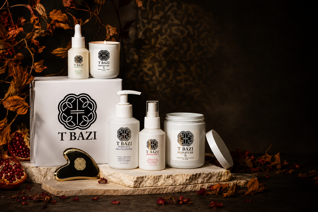 A T Bazi skincare and body care collection displayed on a stone slab with autumn leaves and dried botanicals. The set includes a white gift box with the T Bazi logo, a small serum bottle, a candle jar, a pump bottle, a spray bottle, a cream jar, and a small round tin, all in white with black and gold branding.
