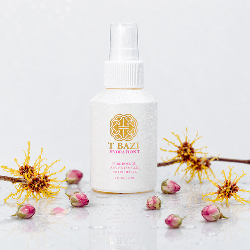 A white spray bottle labeled 'T BAZI HYDRATION T' stands centered on a glossy white surface, surrounded by yellow flowers and pink rose buds against a bright white background.